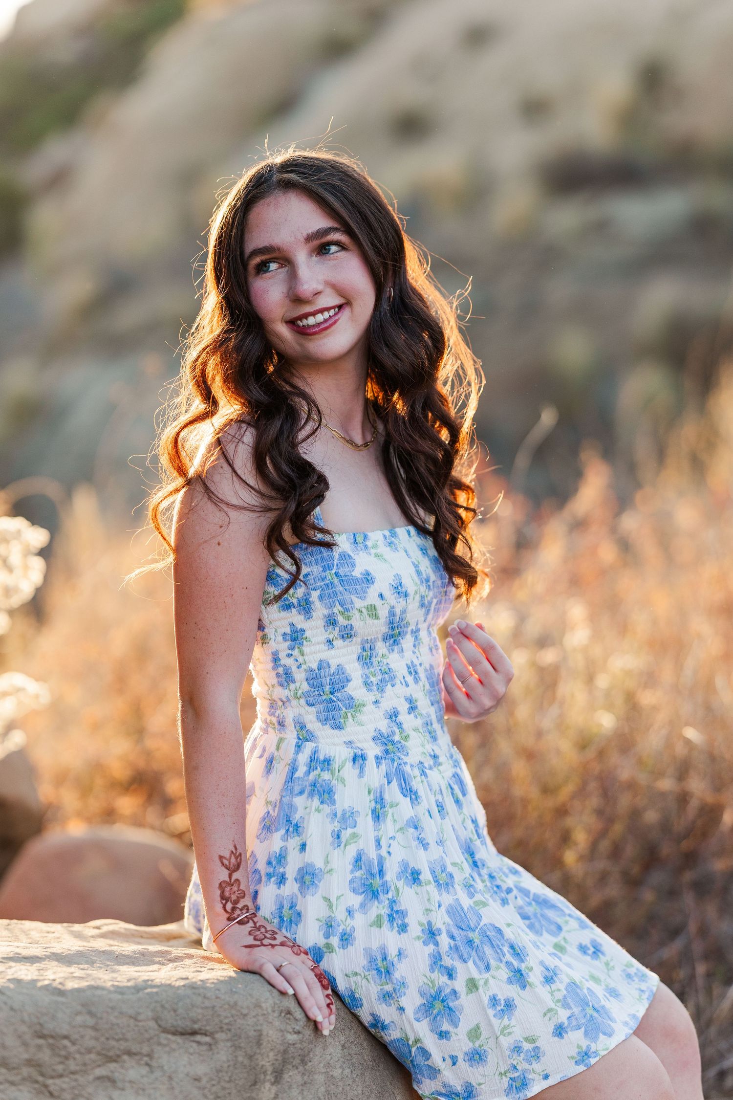 Two friends in blue outfits sit together on rocky ledge during golden hour sunset.