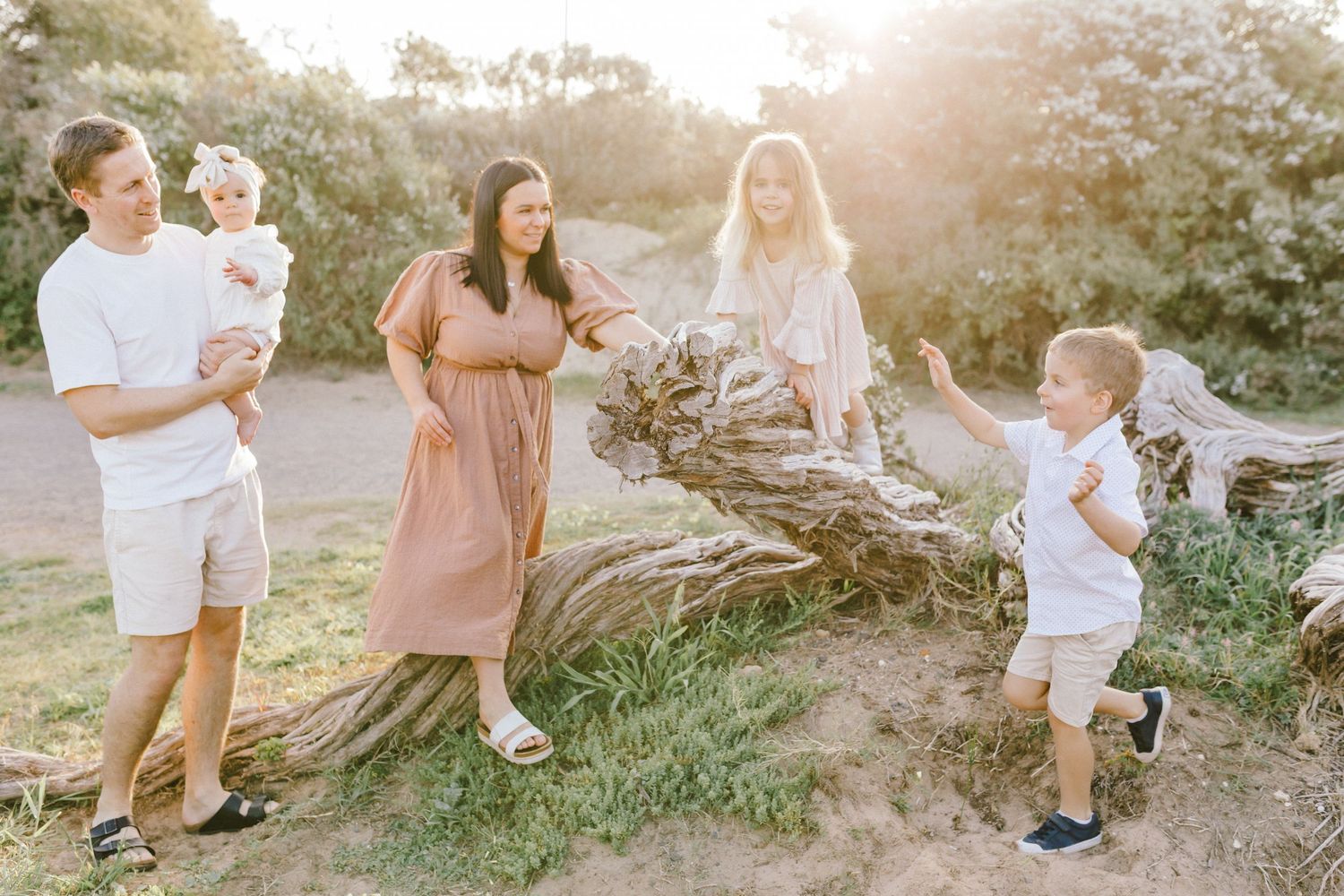 A family enjoys a sunset photoshoot together on a grassy hillside path during golden hour.