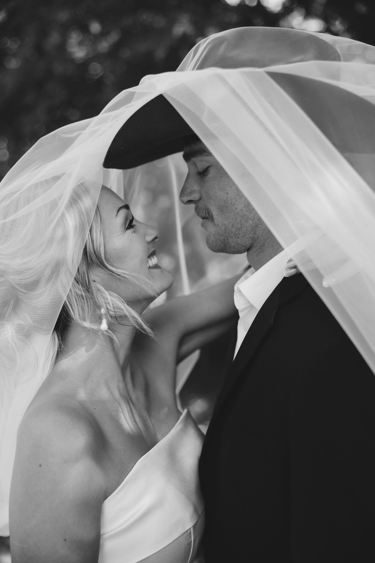 A romantic black and white wedding photo series showing intimate moments between newlyweds under a flowing veil.