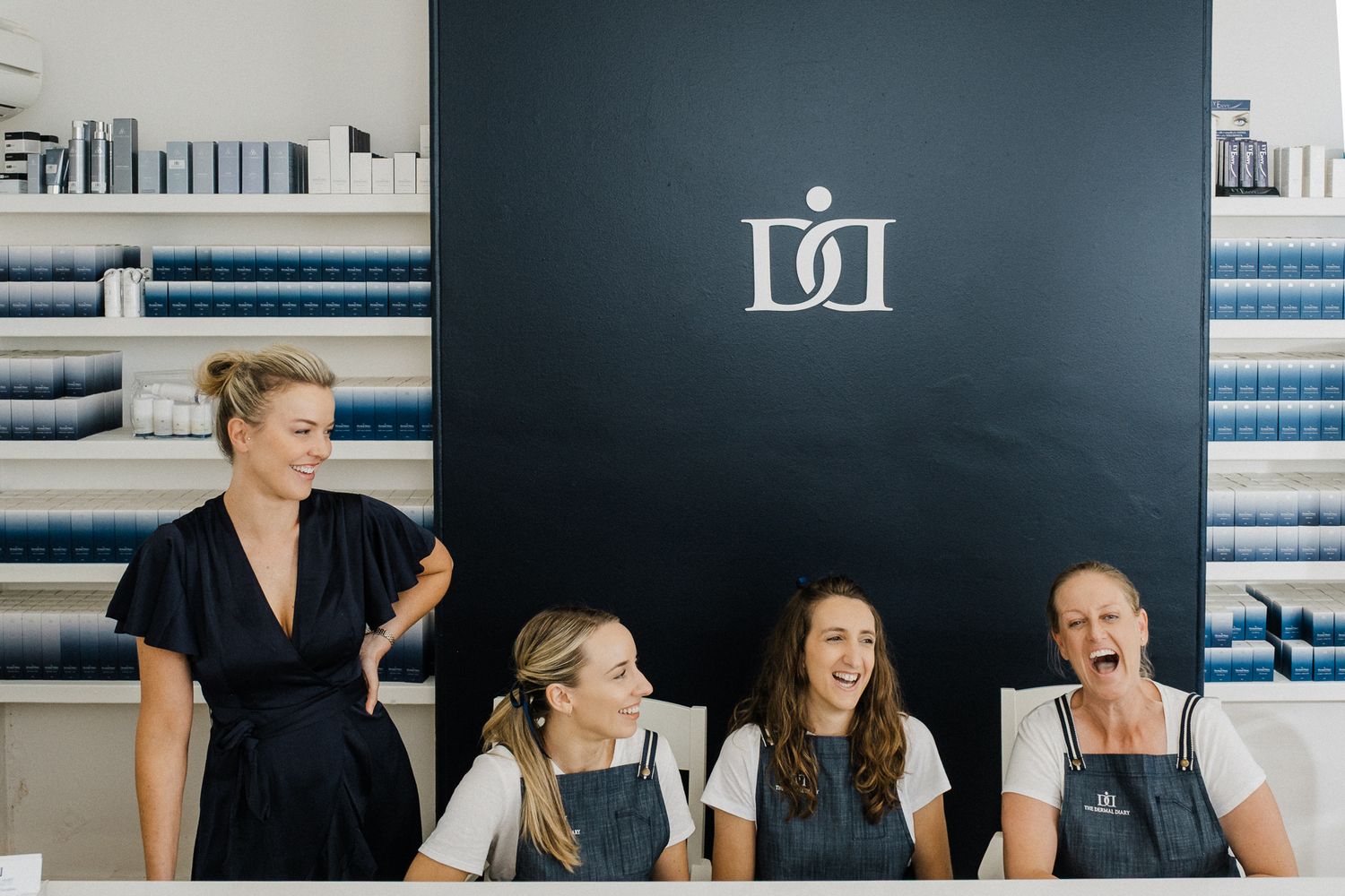 Group of women sharing a lighthearted moment against dark wall with business logo.