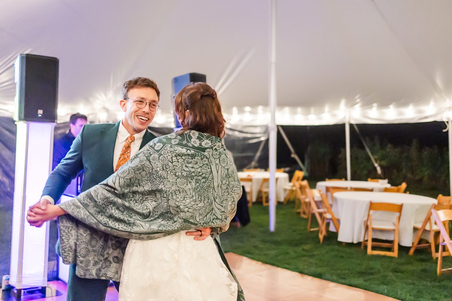 A couple performs a romantic dance dip move during a wedding reception under a white tent with string lights.