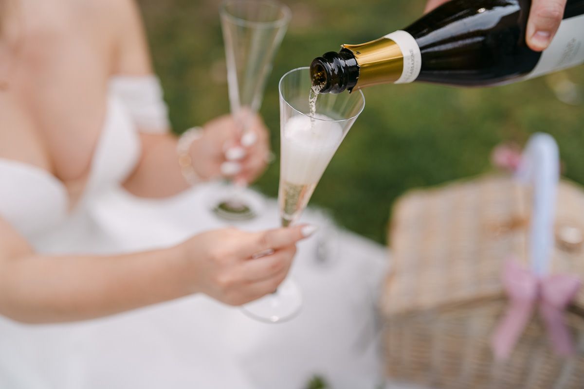 Brautpaar mit Champagnerflasche und Gläsern während eines Editorial-Fotoshootings im Elisengarten in Aachen.