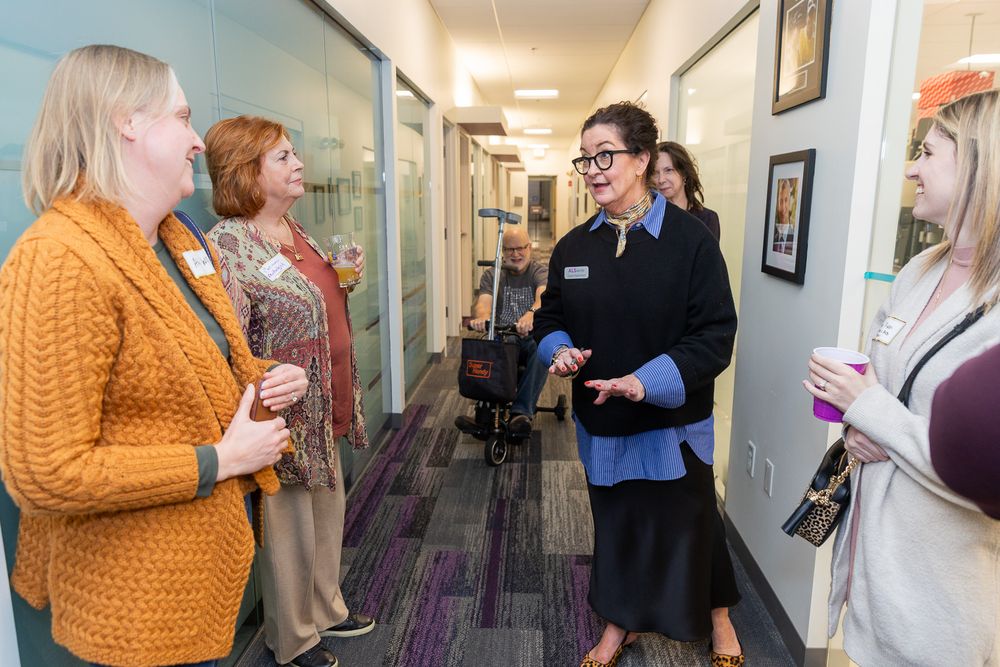 People viewing artwork displayed in a gallery hallway with purple carpeting and white walls.