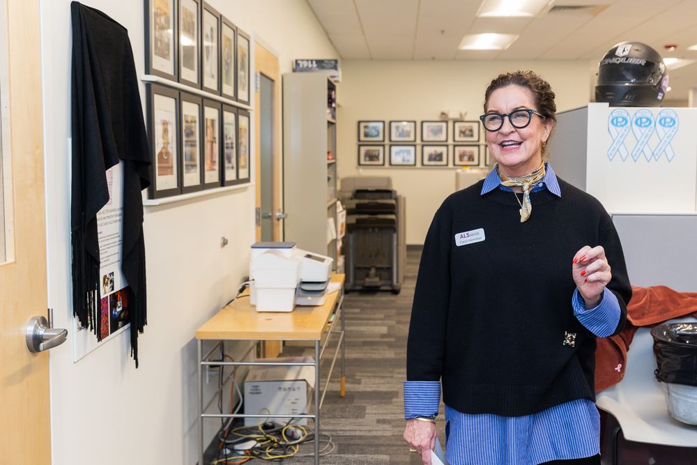 Medical staff in scrubs and lab coats collaborate in a bright hospital hallway with framed photos on the wall.