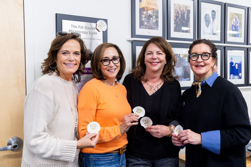 A group of people gather together in an office setting with framed photos on the wall behind them.