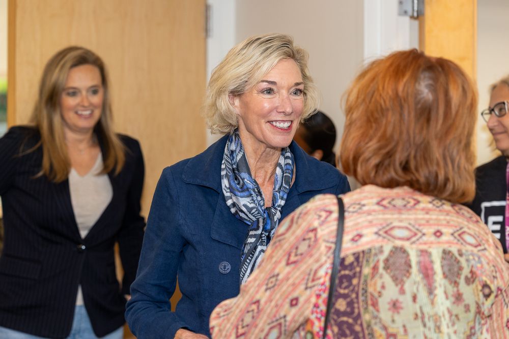 People in a meeting room share smiles and conversations during a professional gathering.