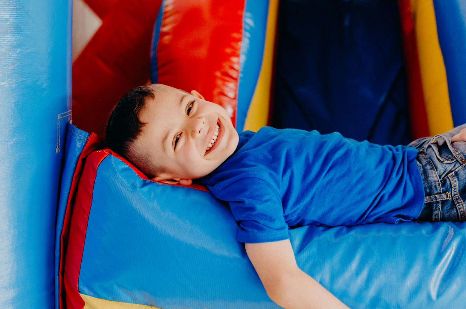 A person in a blue shirt lies down on a red and blue inflatable bounce house surface.
