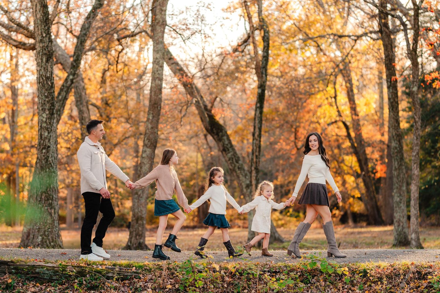 Family walking through autumn leaves in coordinated outfits during a fall photoshoot in the woods.