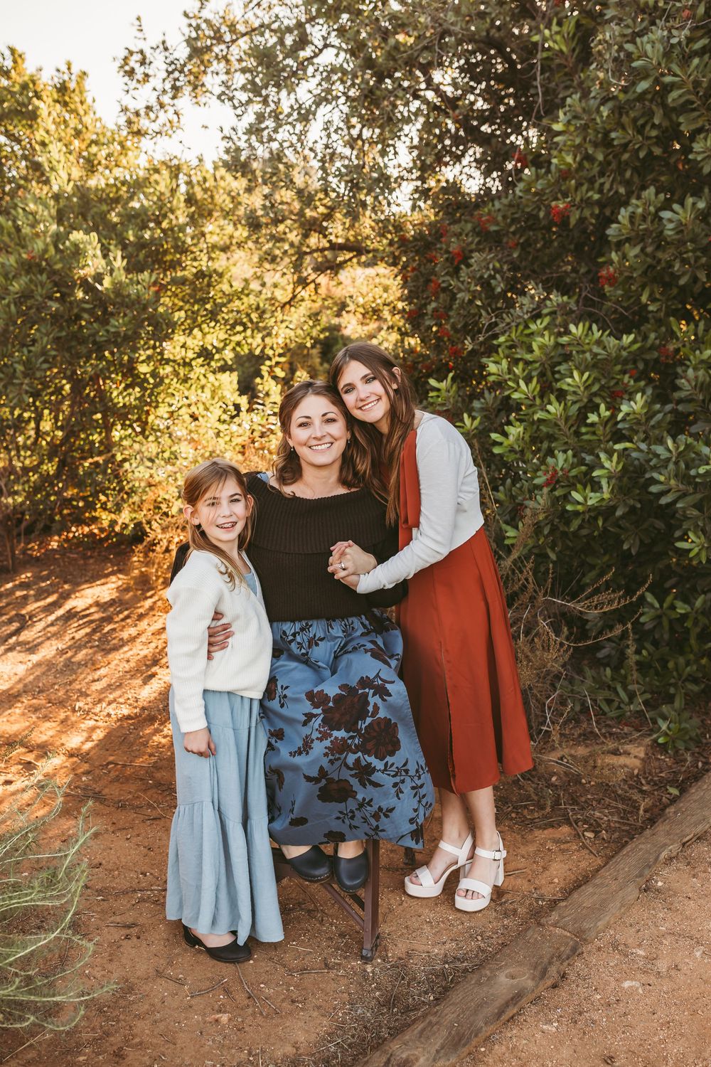 Family members pose together on a dirt path surrounded by lush greenery in warm evening light.