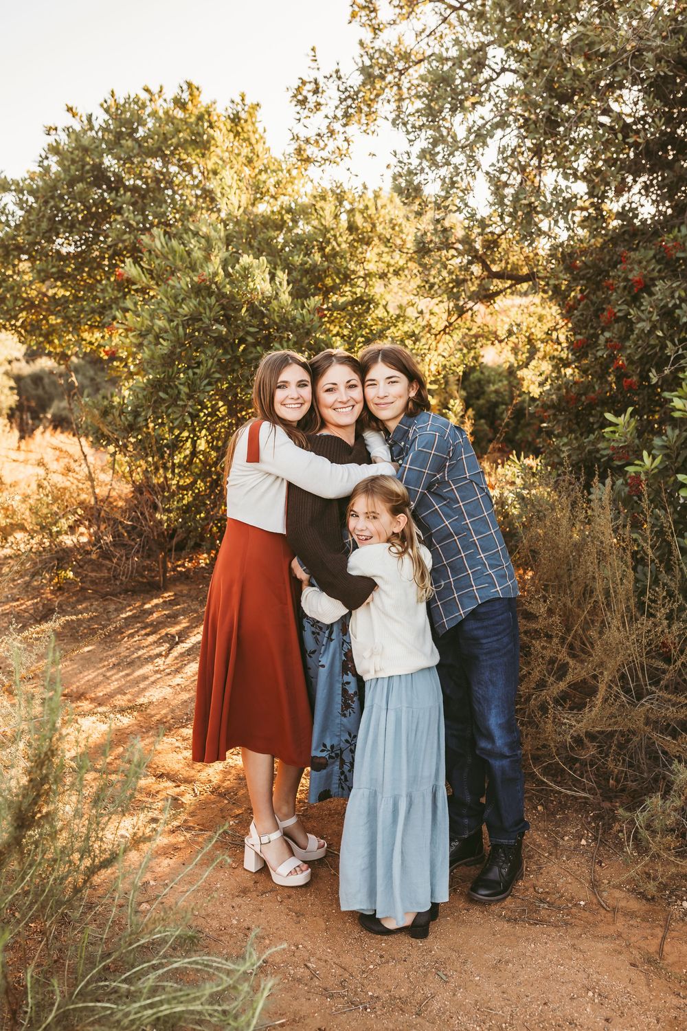 A family poses together on a dirt trail during golden hour with trees and foliage in the background.