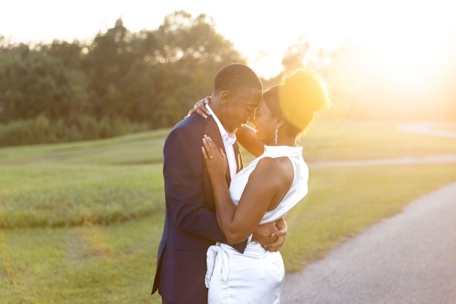 Romantic couple embracing and kissing at sunset on a scenic golf course pathway.