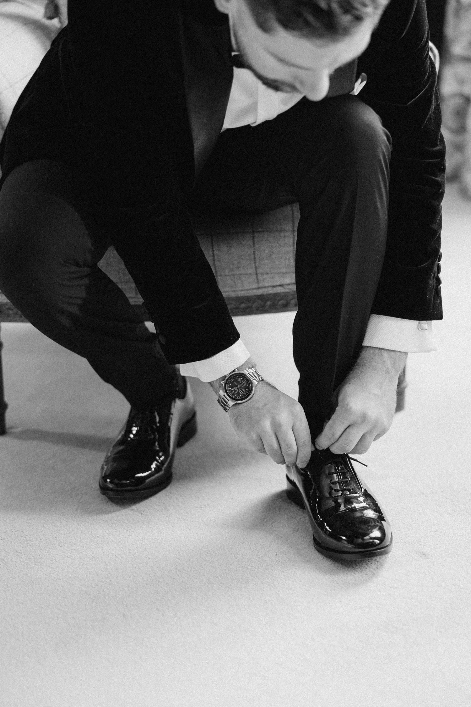 Close-up of formal black dress shoes being tied on white floor.