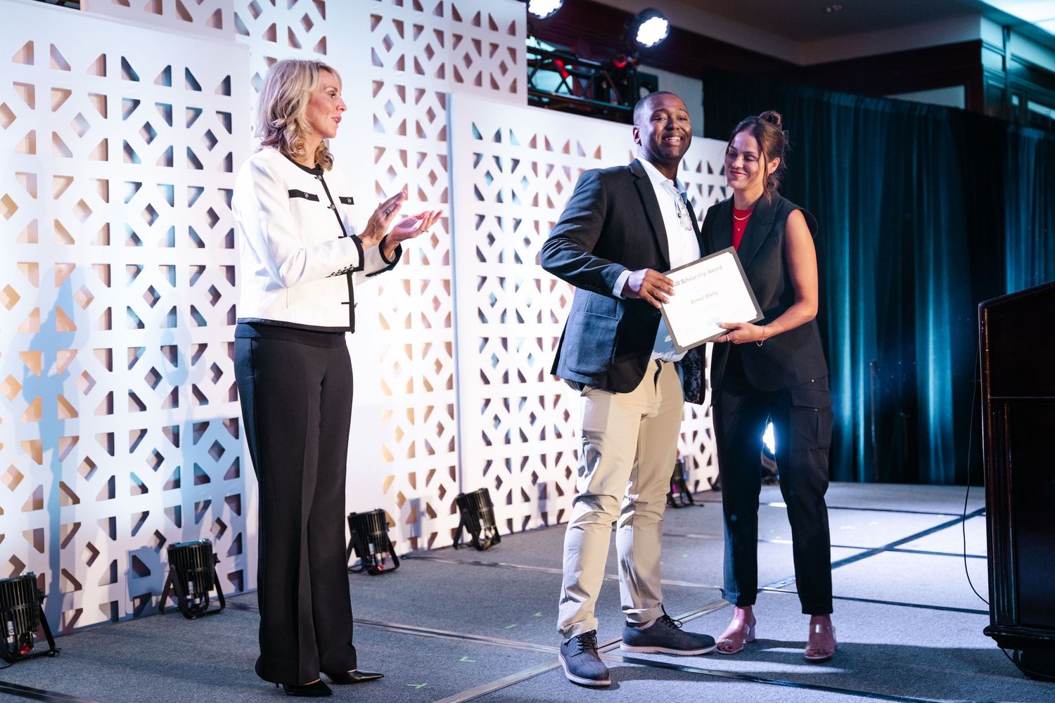 People interact on stage during a presentation at a business conference with geometric patterned backdrop.