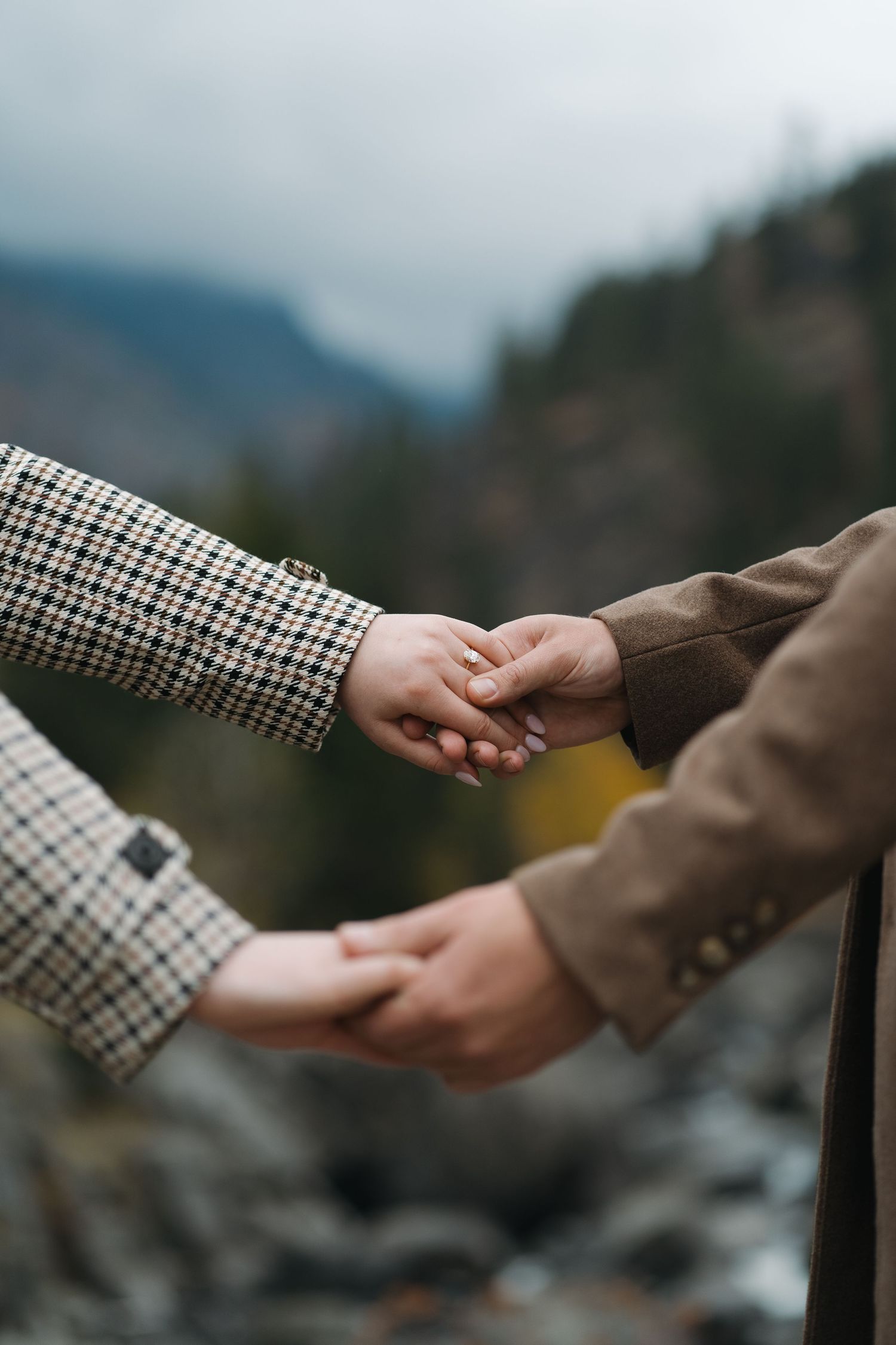 Two people holding hands tenderly against a misty mountain landscape with a river in the background.