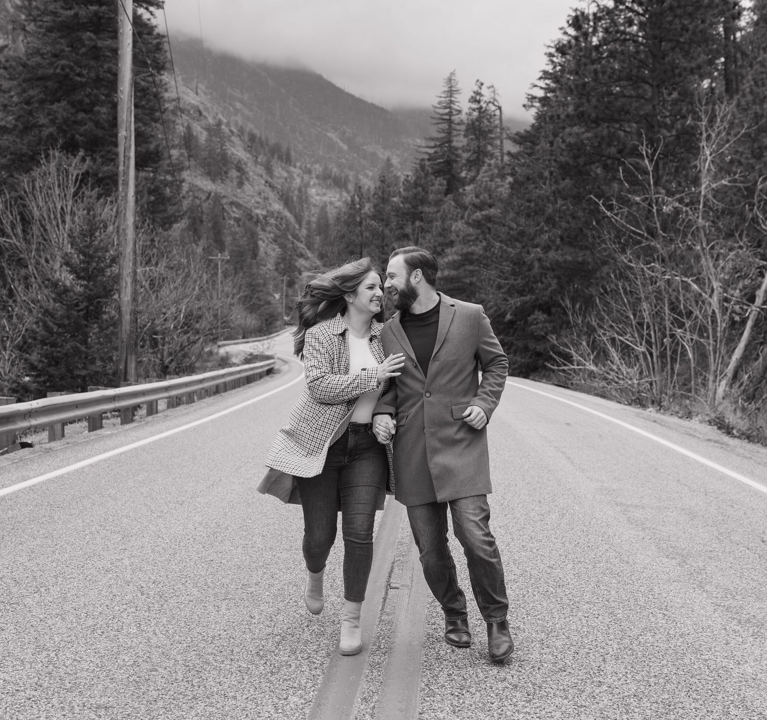 A couple shares an intimate moment together on a mountain road surrounded by evergreen trees and scenic views.