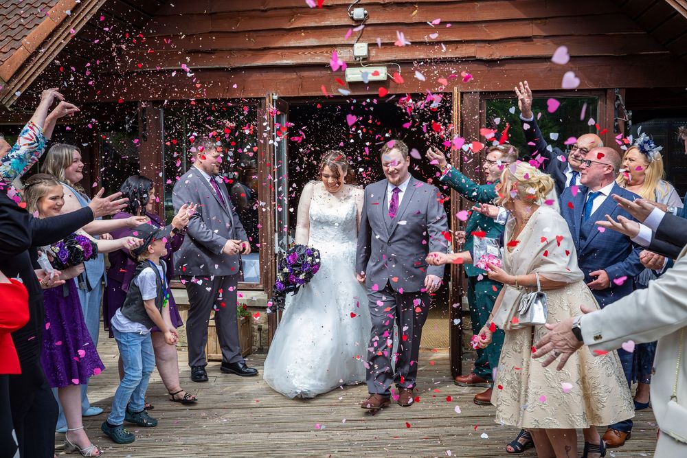 Newlywed couple exits wedding venue through a joyful shower of colorful confetti thrown by smiling guests.