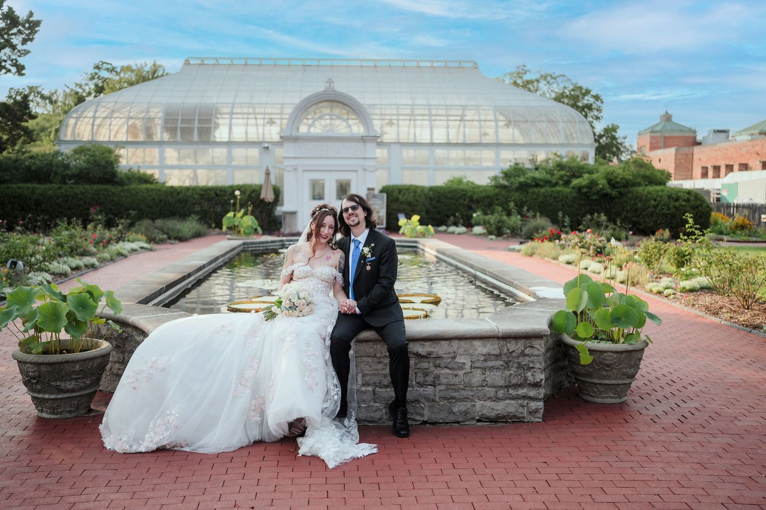 Toledo Zoo & Aquarium Wedding party poses in front of a greenhouse conservatory with elegant white floral arrangements.