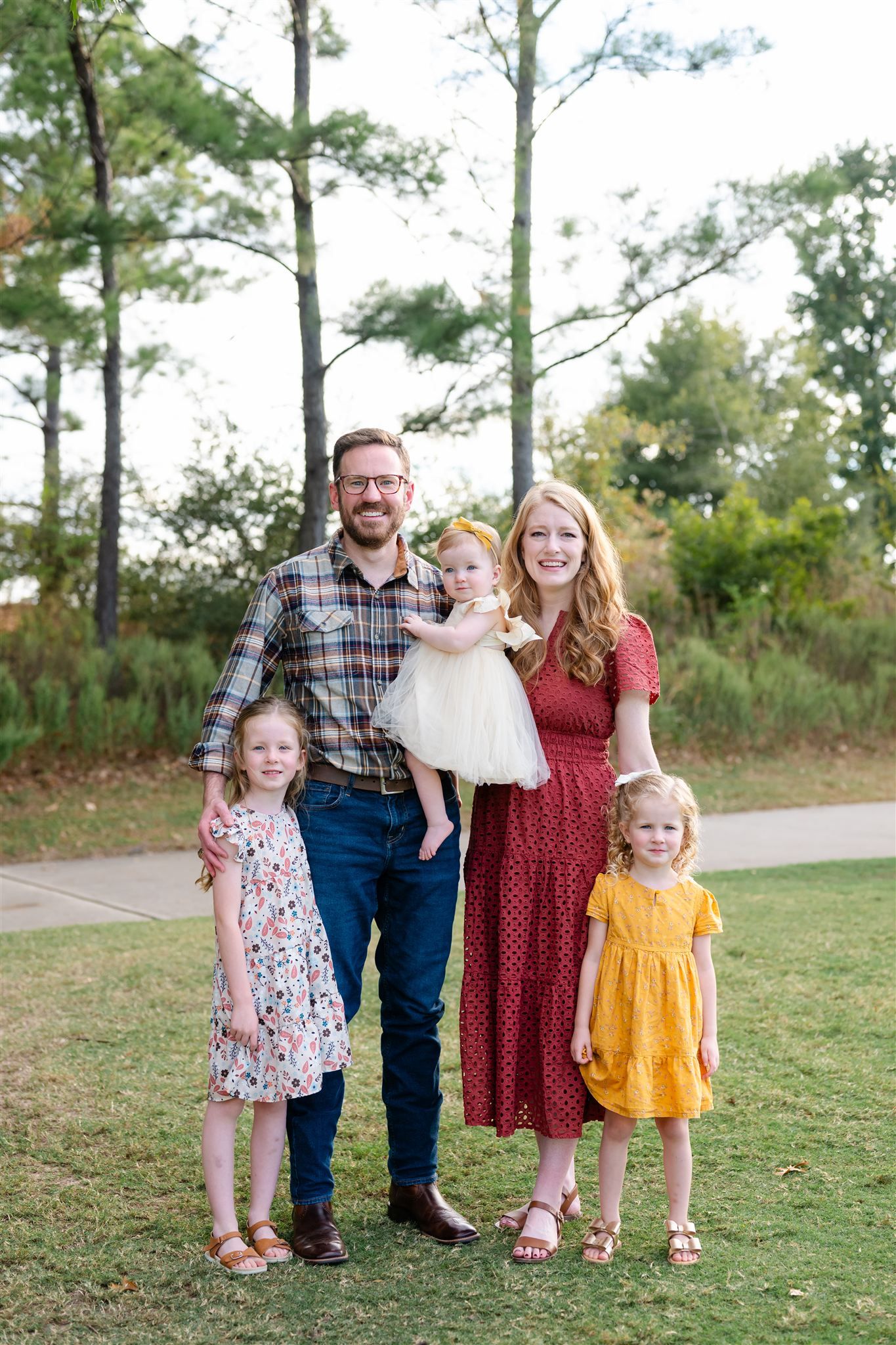 Family in coordinated outfits poses together on a grassy hill with pine trees in the background.