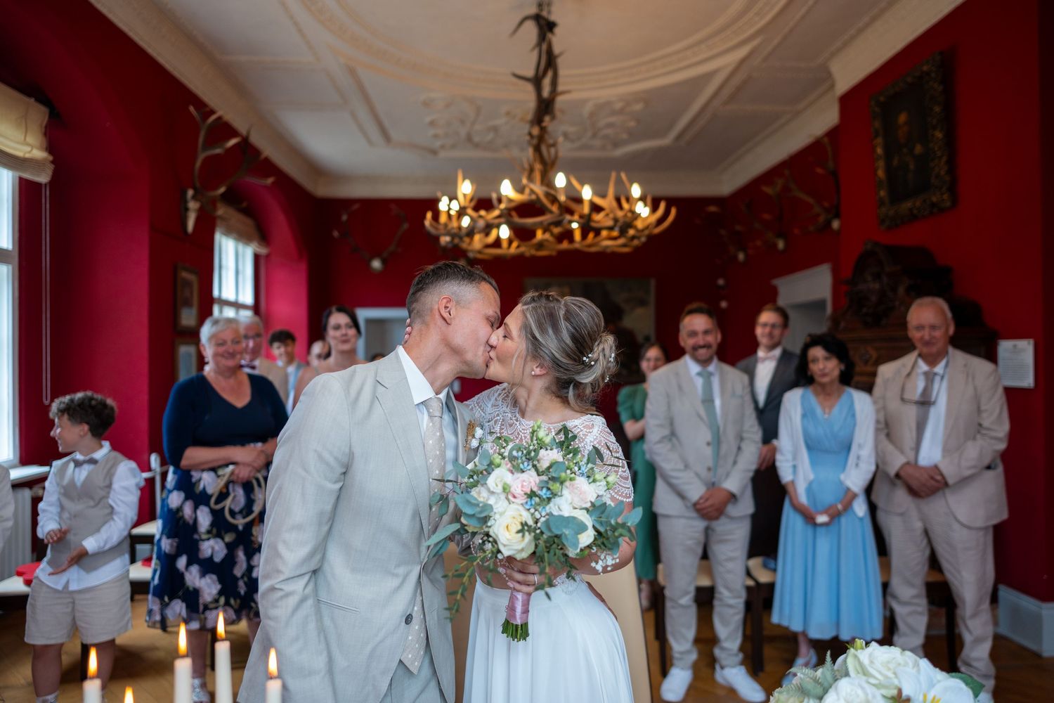 Ein formell gekleidetes Brautpaar posiert vor einem prächtigen gelben Herrenhaus mit weißen Verzierungen an ihrem Hochzeitstag.