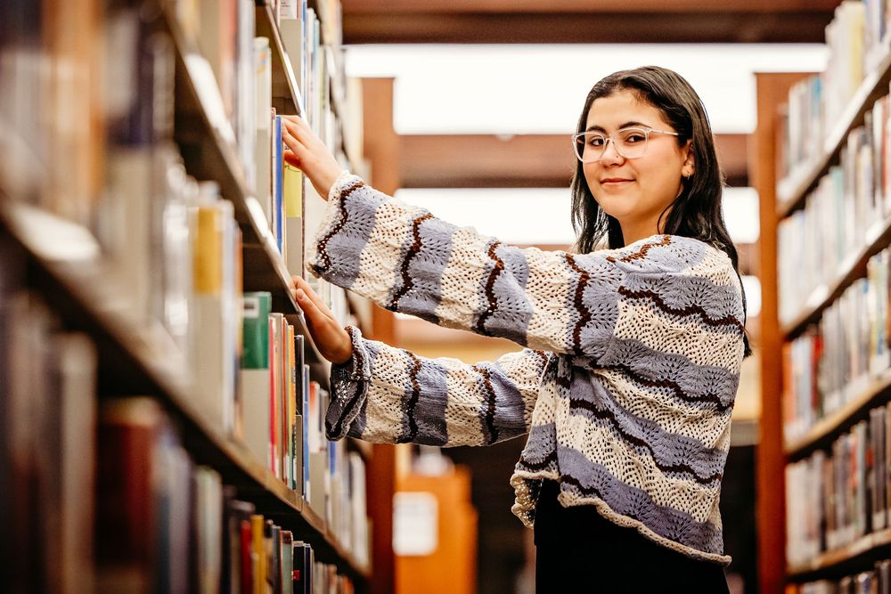 A person reaches for a book while browsing through library shelves filled with various titles.