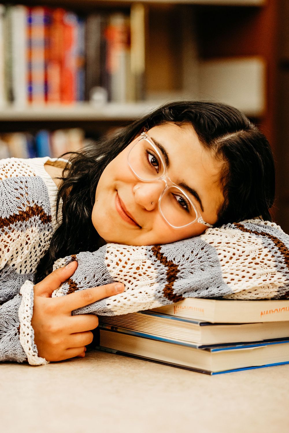 Student rests head on textbooks while studying in library with cozy white knit sweater.