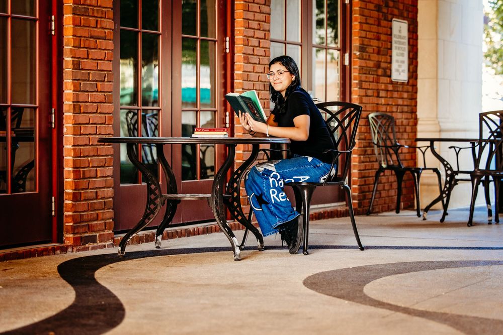 A person sits on a porch with red brick walls and black metal railings in front of a glass door.