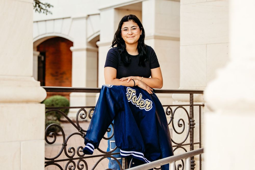 A person wearing a navy blue UCLA sweatshirt poses on an elegant white stone staircase with ornate iron railings.