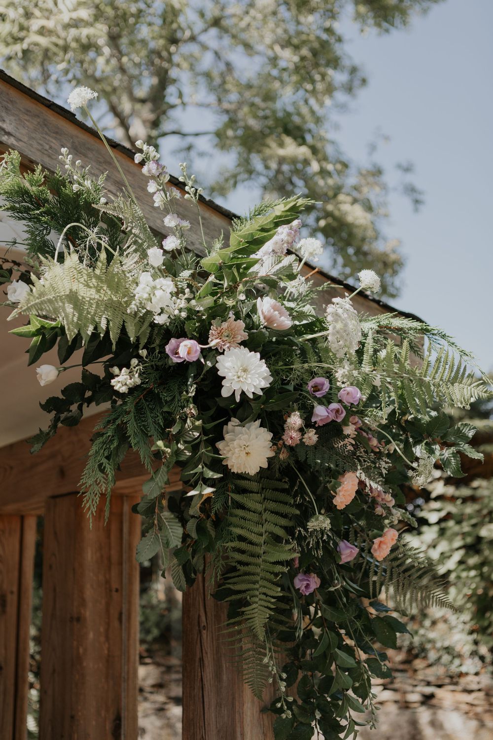 Lush floral arch with ferns, white dahlias, and pink blooms decorating a rustic wooden structure.