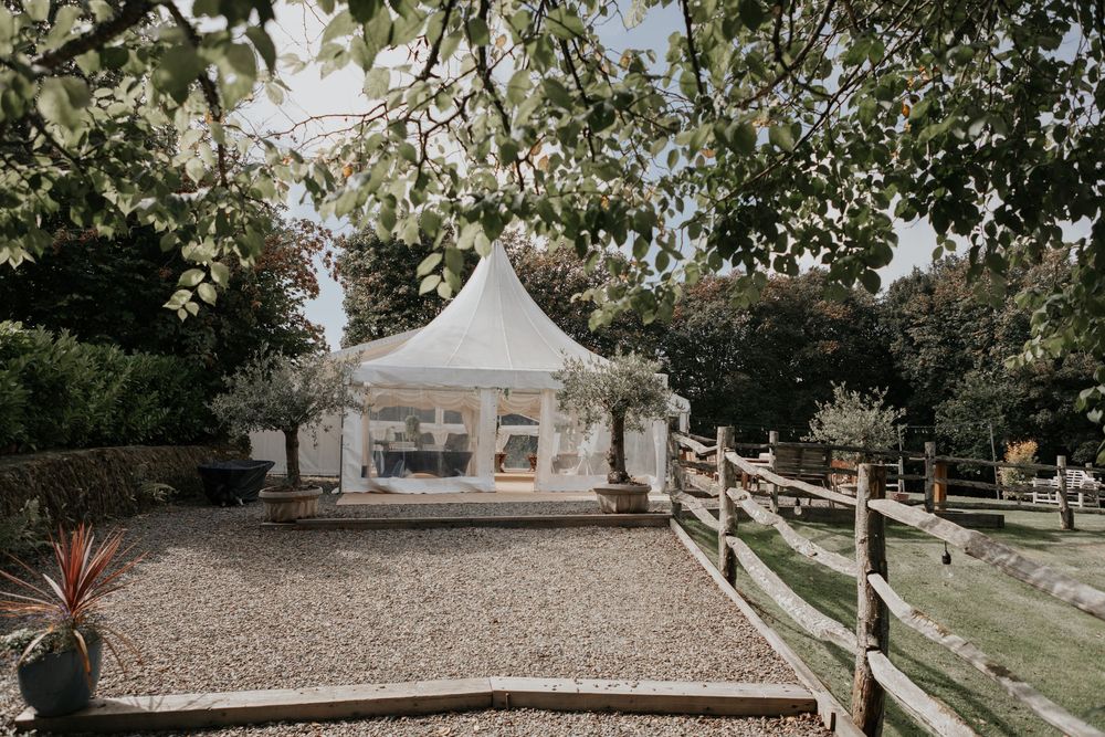 White pagoda marquee wedding tent with wooden fencing and mature trees at countryside venue.