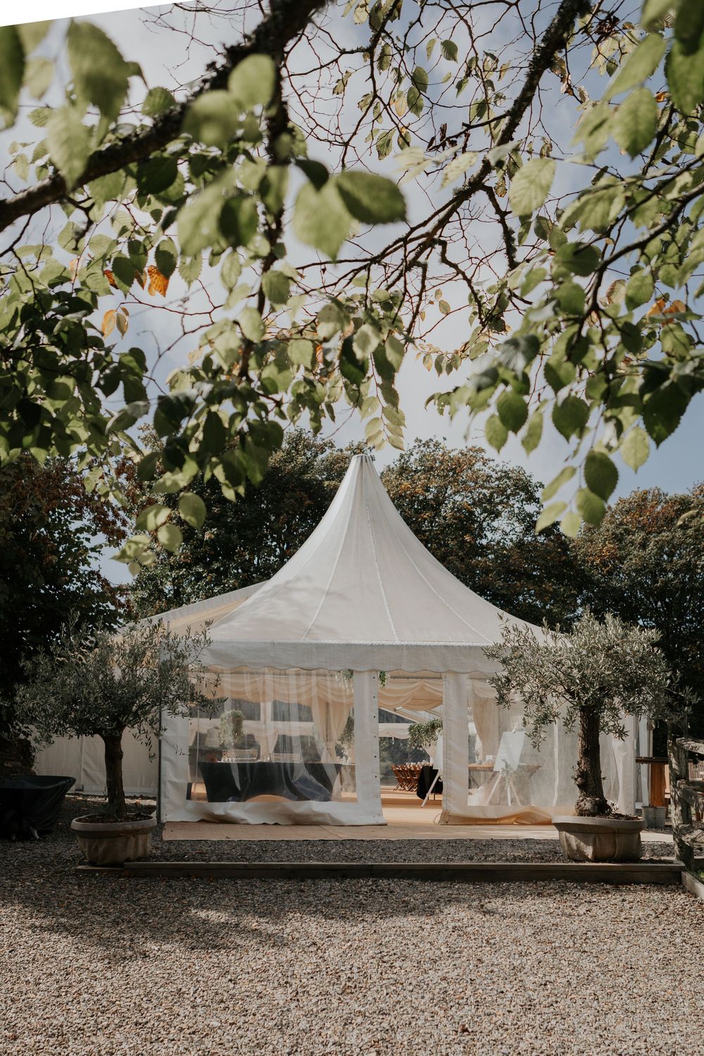 Elegant white pagoda marquee tent surrounded by trees and gravel at outdoor wedding venue.