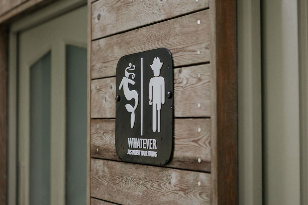 Quirky gender-neutral bathroom sign reading Whatever on rustic wooden wall.