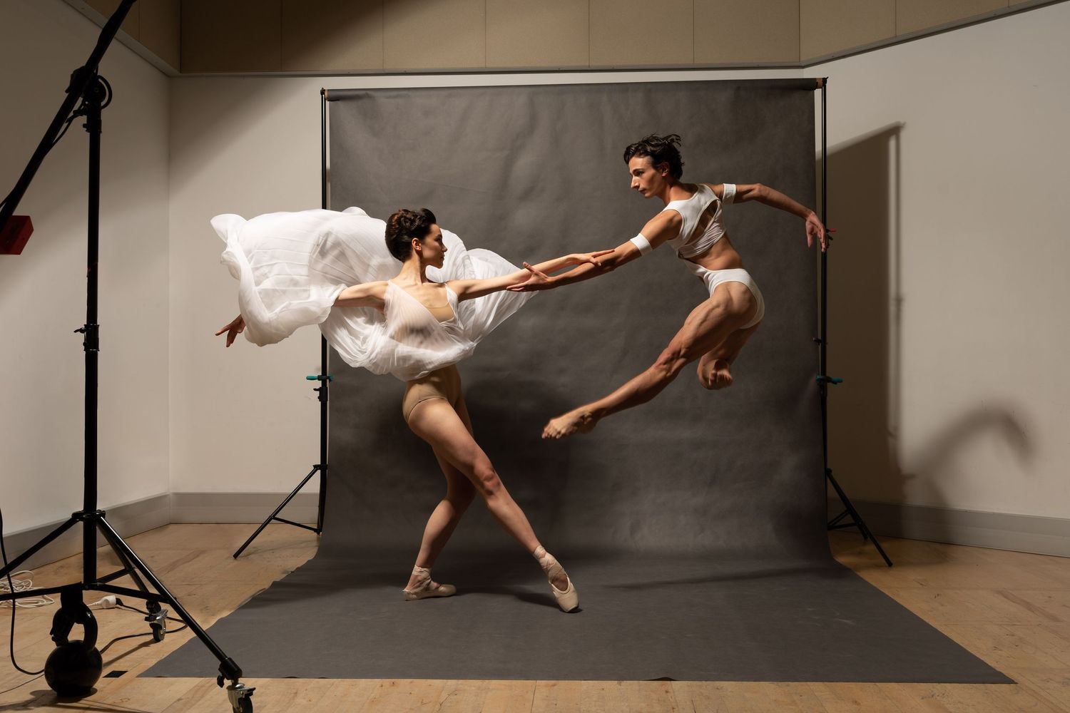 Two ballet dancers leap and spin gracefully during a professional photo shoot in a studio.
