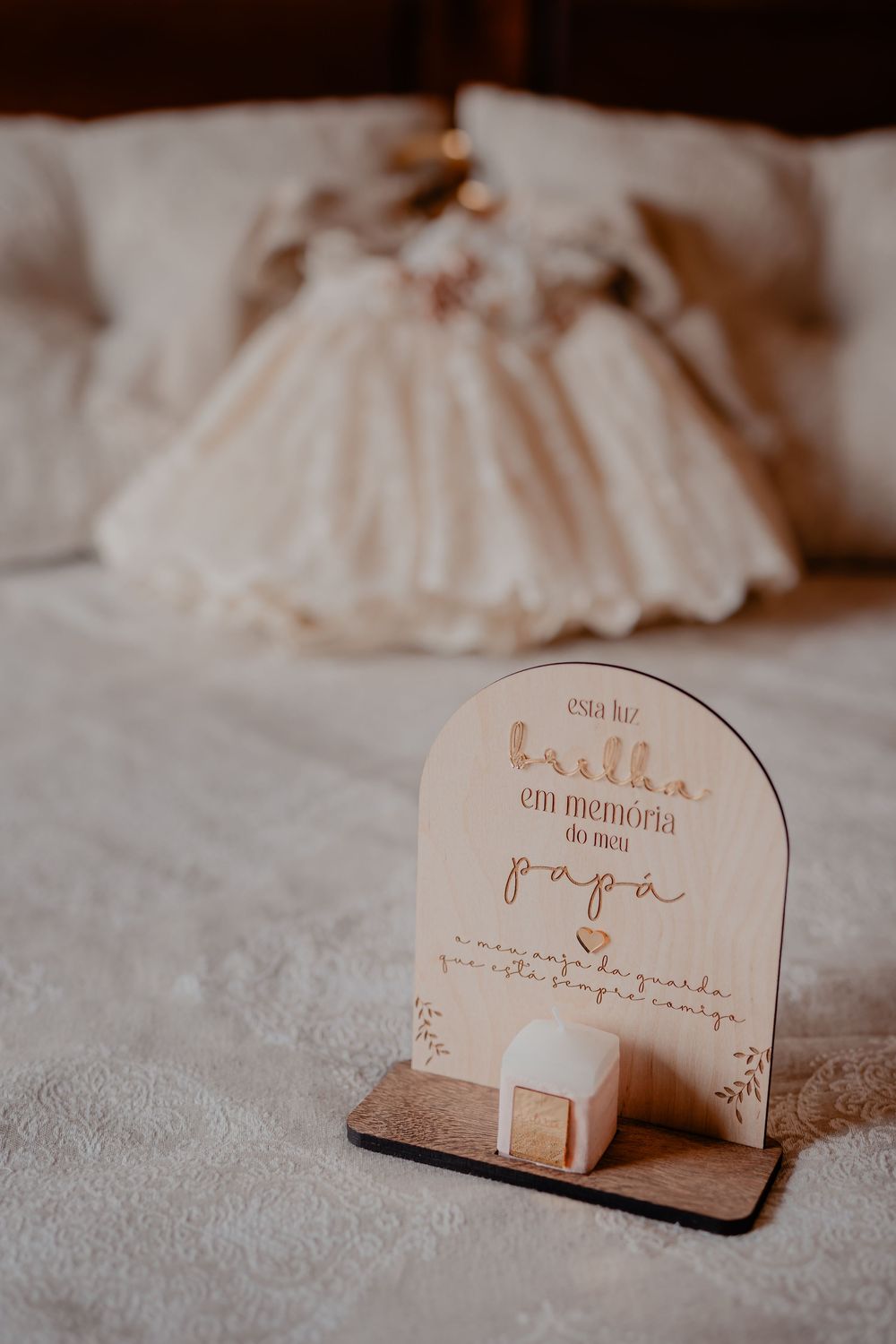 A delicate christening or baptism dress displayed on a bed with a decorative wooden sign.
