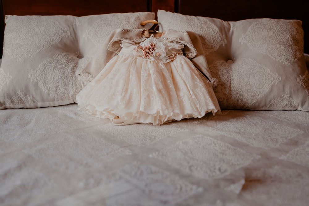 A beautiful white baptismal or christening dress arranged on a bed with pillows.