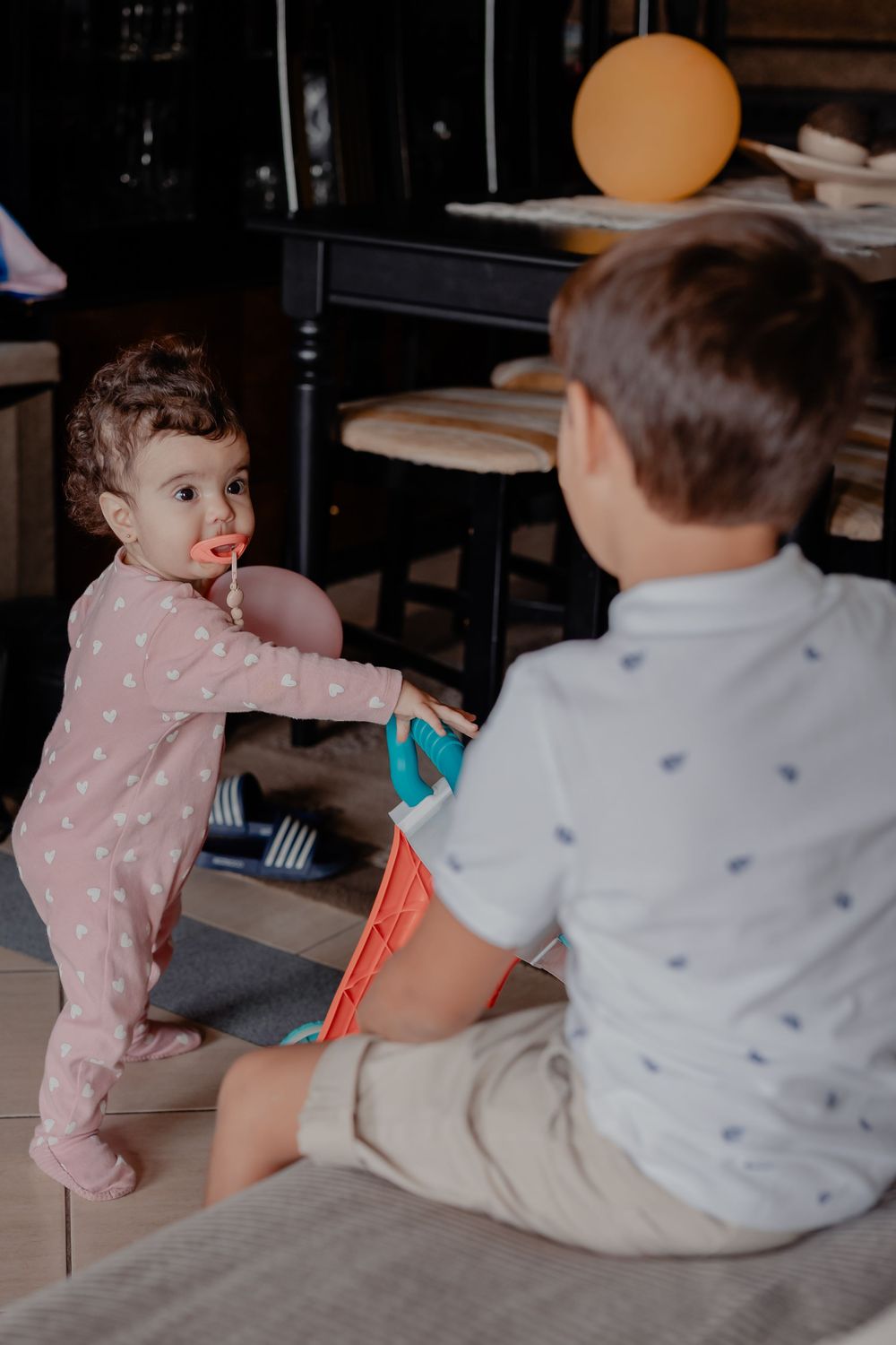Two small children play together on a dark wooden floor in casual clothing.