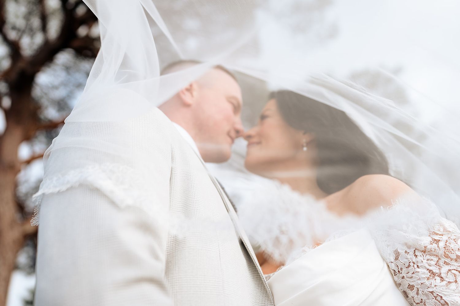 A romantic moment captured through flowing white wedding veil against soft light.