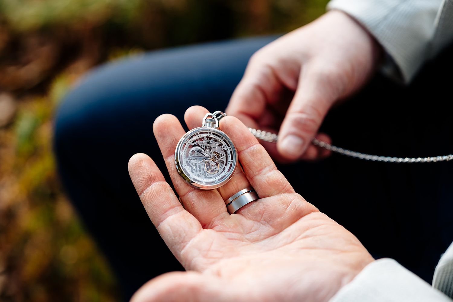A close-up view of silver wedding rings being exchanged during an outdoor ceremony.