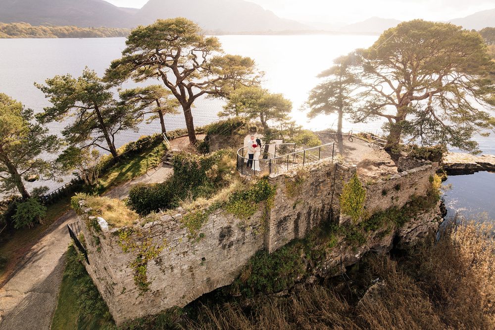 Scenic cliffside view of Killarney National Park in Ireland with ancient stone ruins and towering pine trees at sunset.