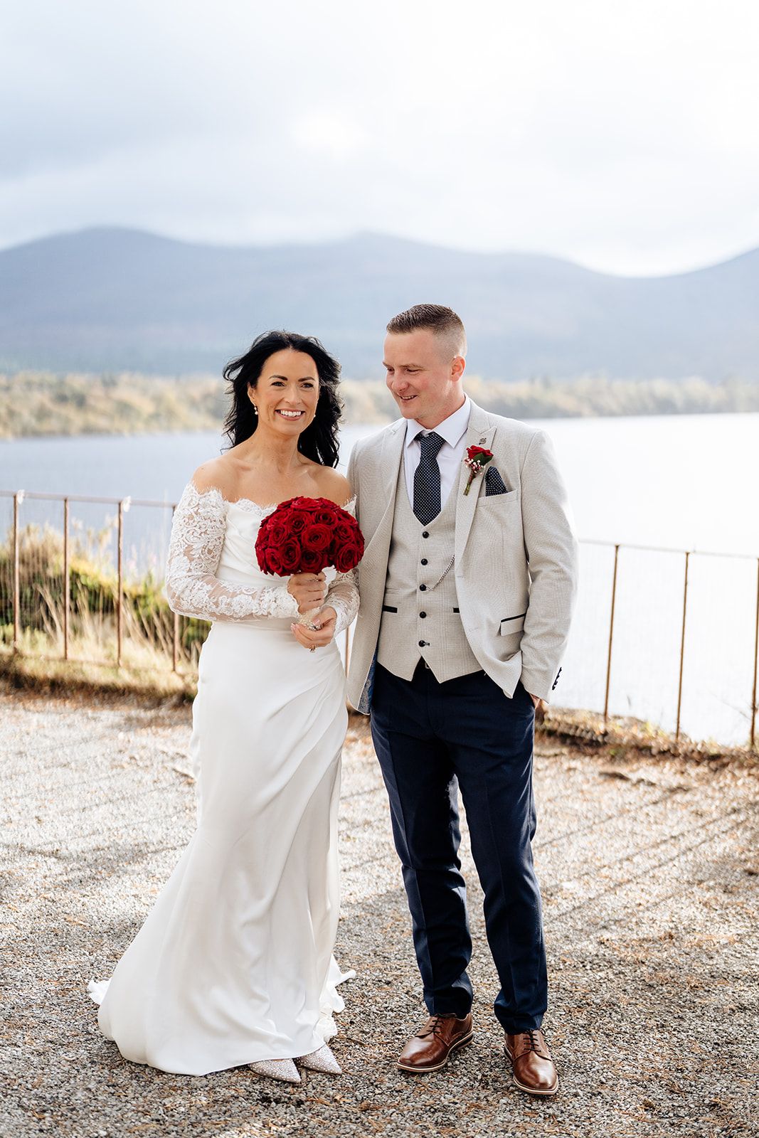 Couple walking and laughing together along a scenic lakeside path on their wedding day.