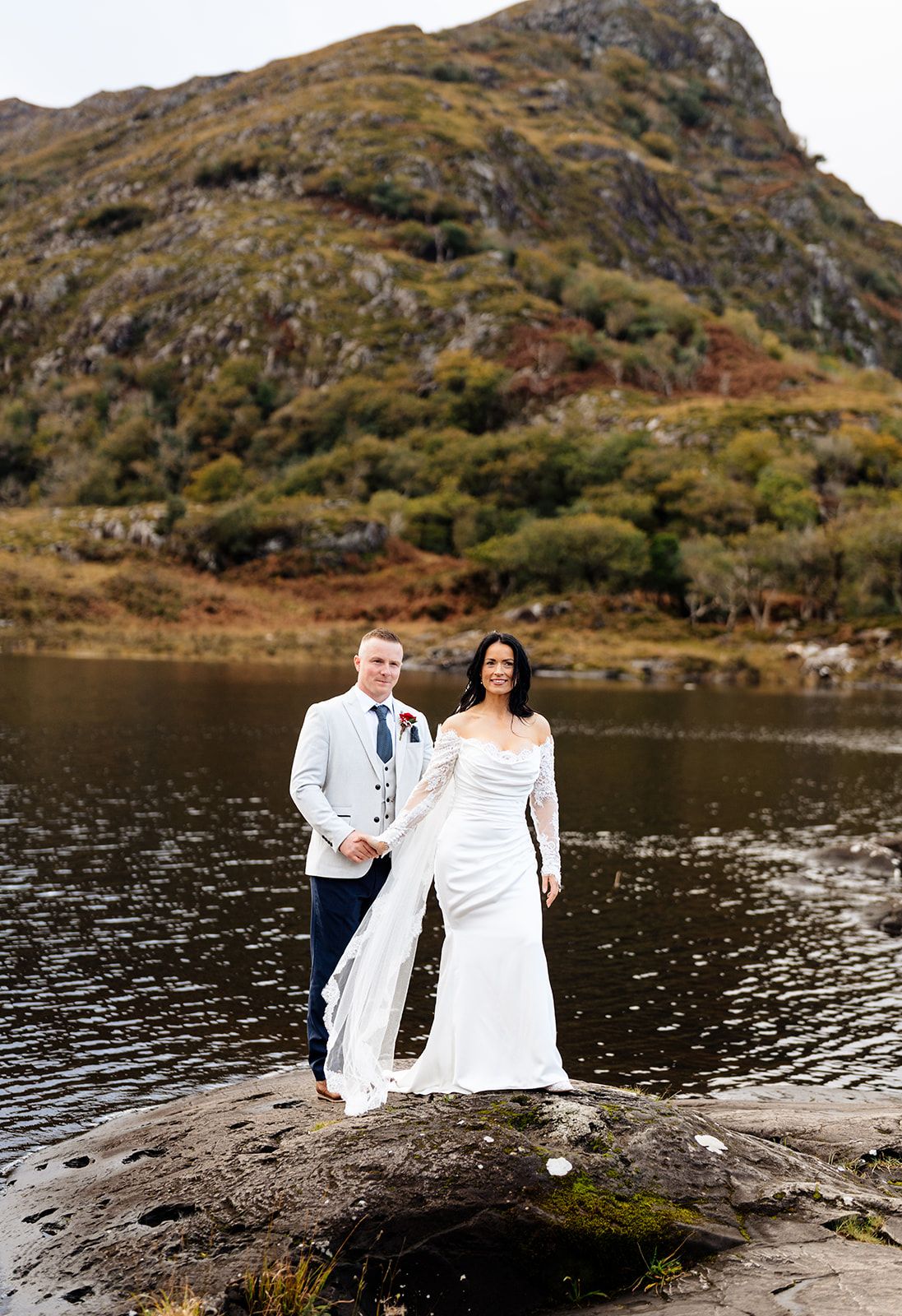 Newlyweds photographed from behind standing by a scenic mountain lake.