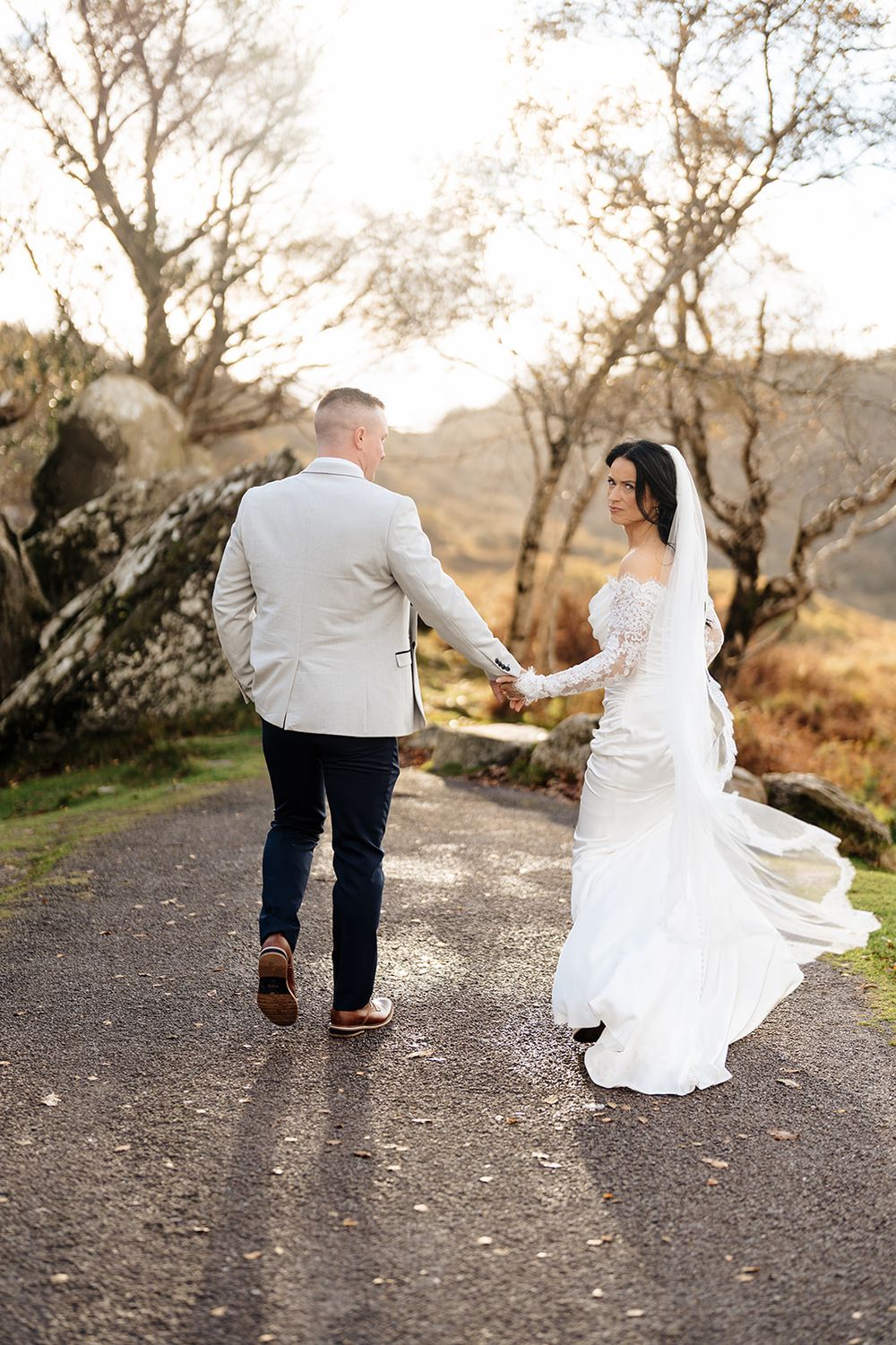 A couple walking away on a path during a wedding photoshoot, with the bride's white dress flowing in motion.