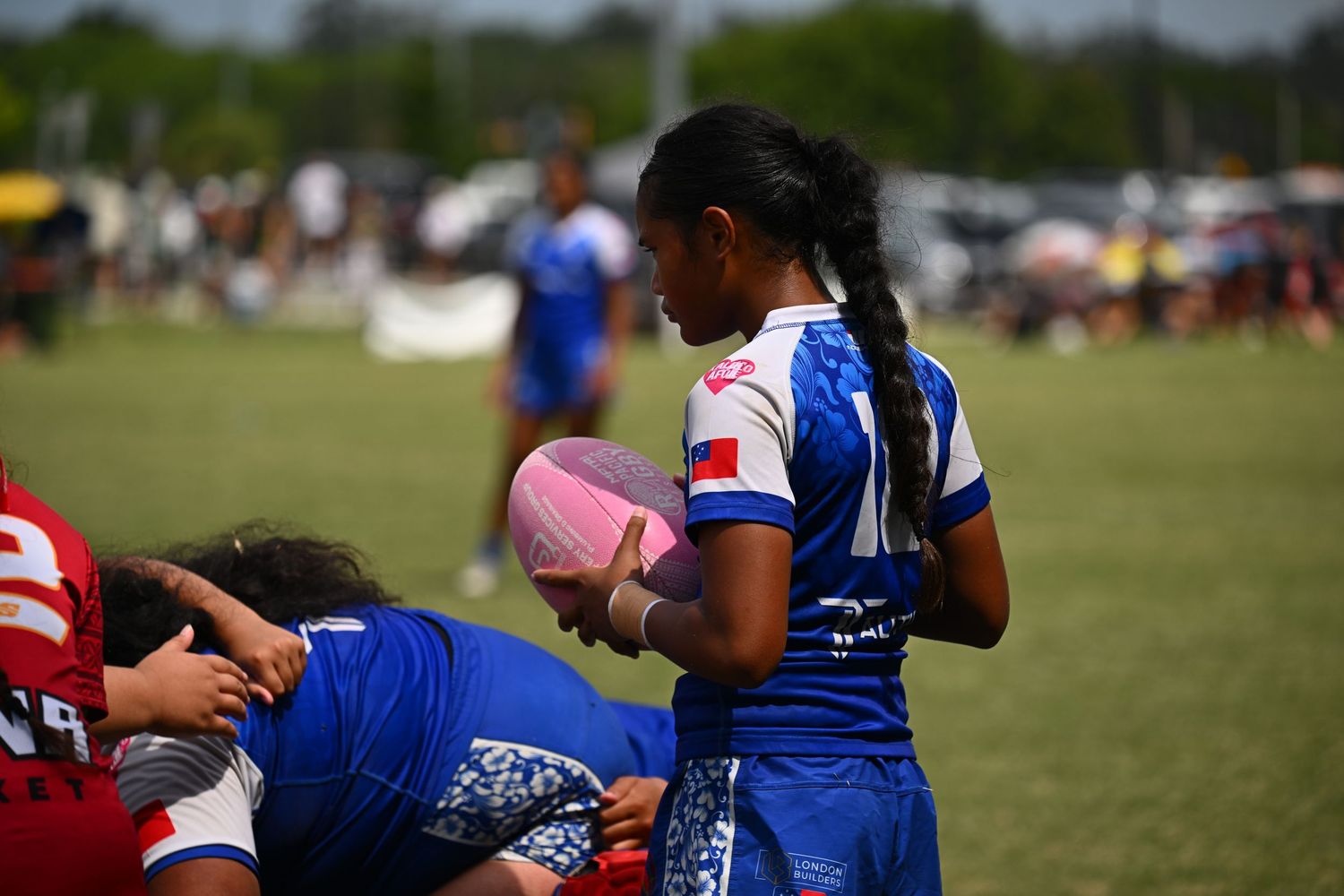 Rugby player in blue jersey holds a pink water bottle during a match on a sunny field.