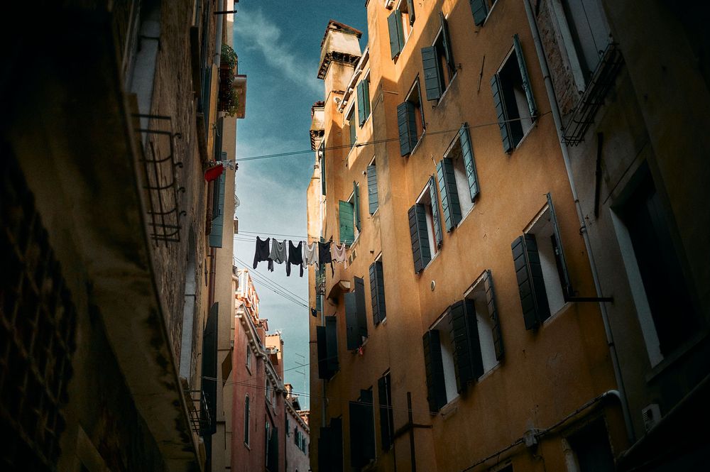 Low angle view of tall apartment buildings in Venice with laundry hanging between balconies against blue sky.