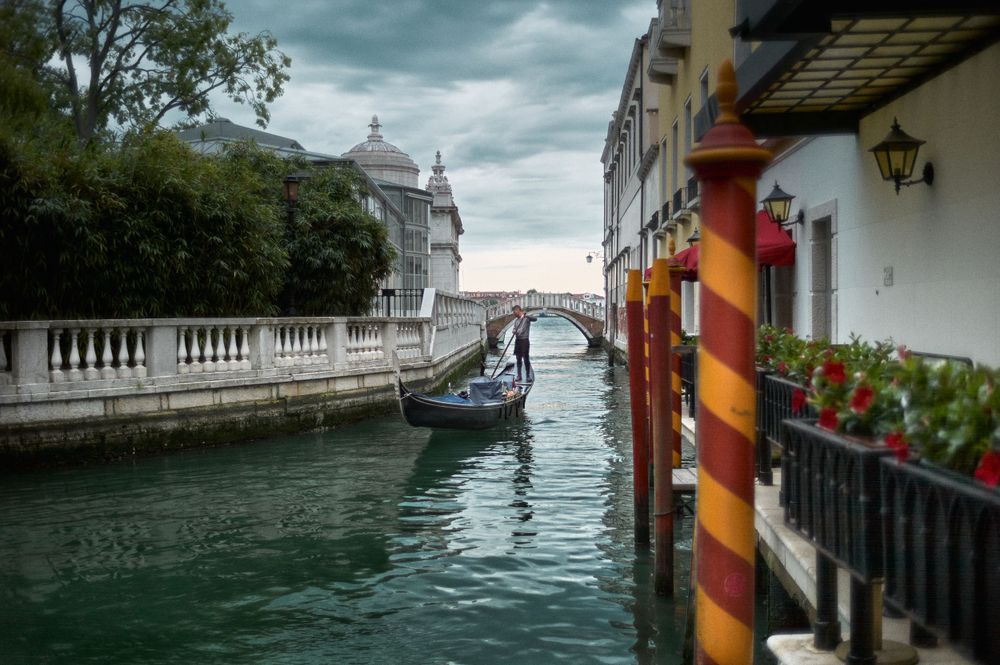 Ornate waterfront buildings and traditional mooring poles line a narrow Venetian canal.