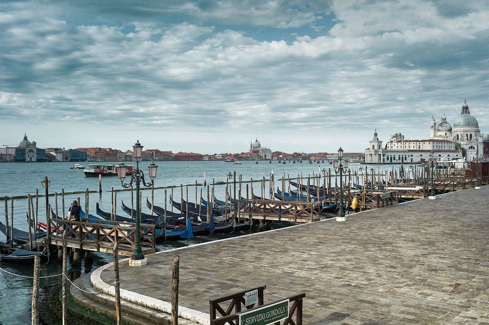 A panoramic view of Venice's iconic waterfront with gondolas and historic buildings under cloudy skies.