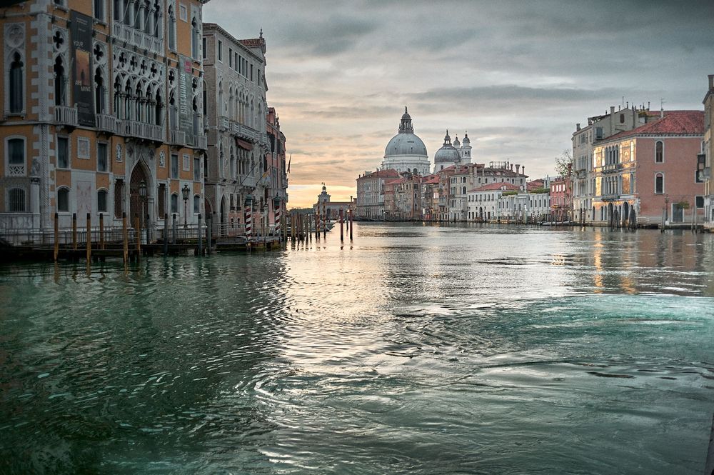 Panoramic view of Venice's Grand Canal with historic buildings and moody cloudy sky at sunset.