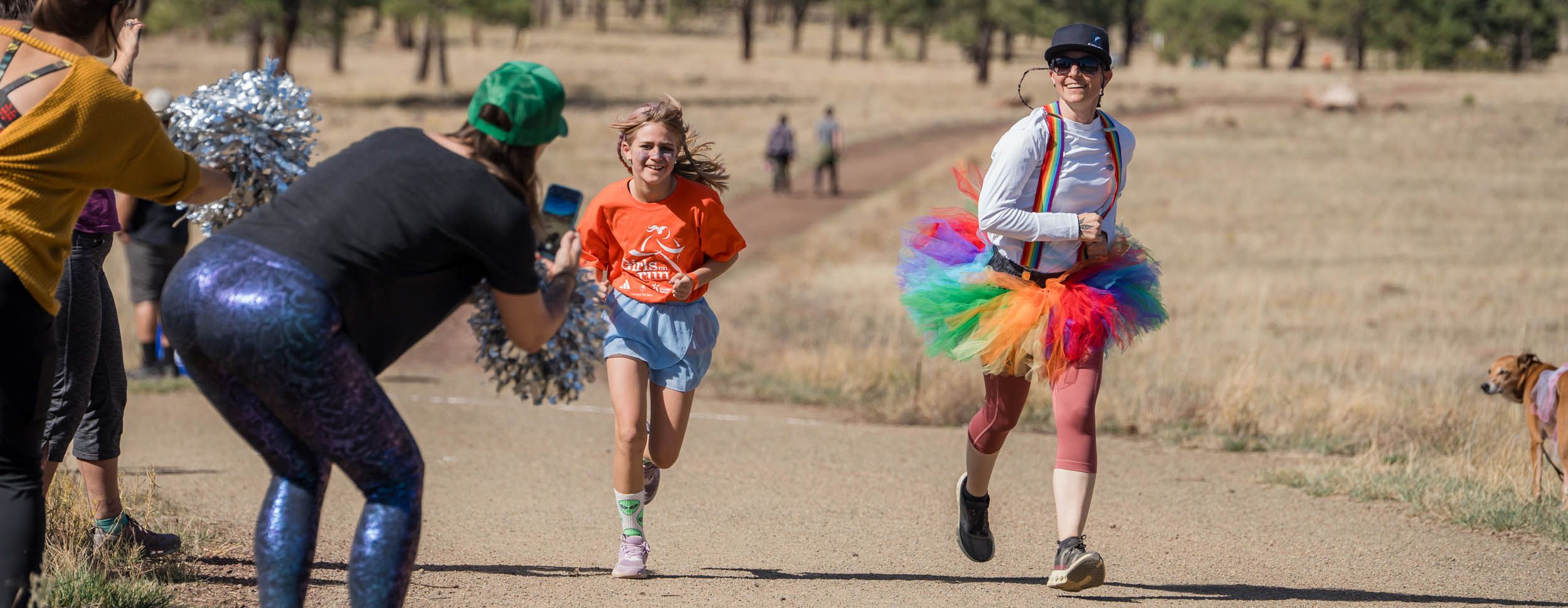 Trail runners compete in a scenic mountain race across rugged desert terrain with mountains in the background.
