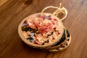 A rustic wooden tray with dried pink flowers and petals arranged artistically on a dark wooden surface.