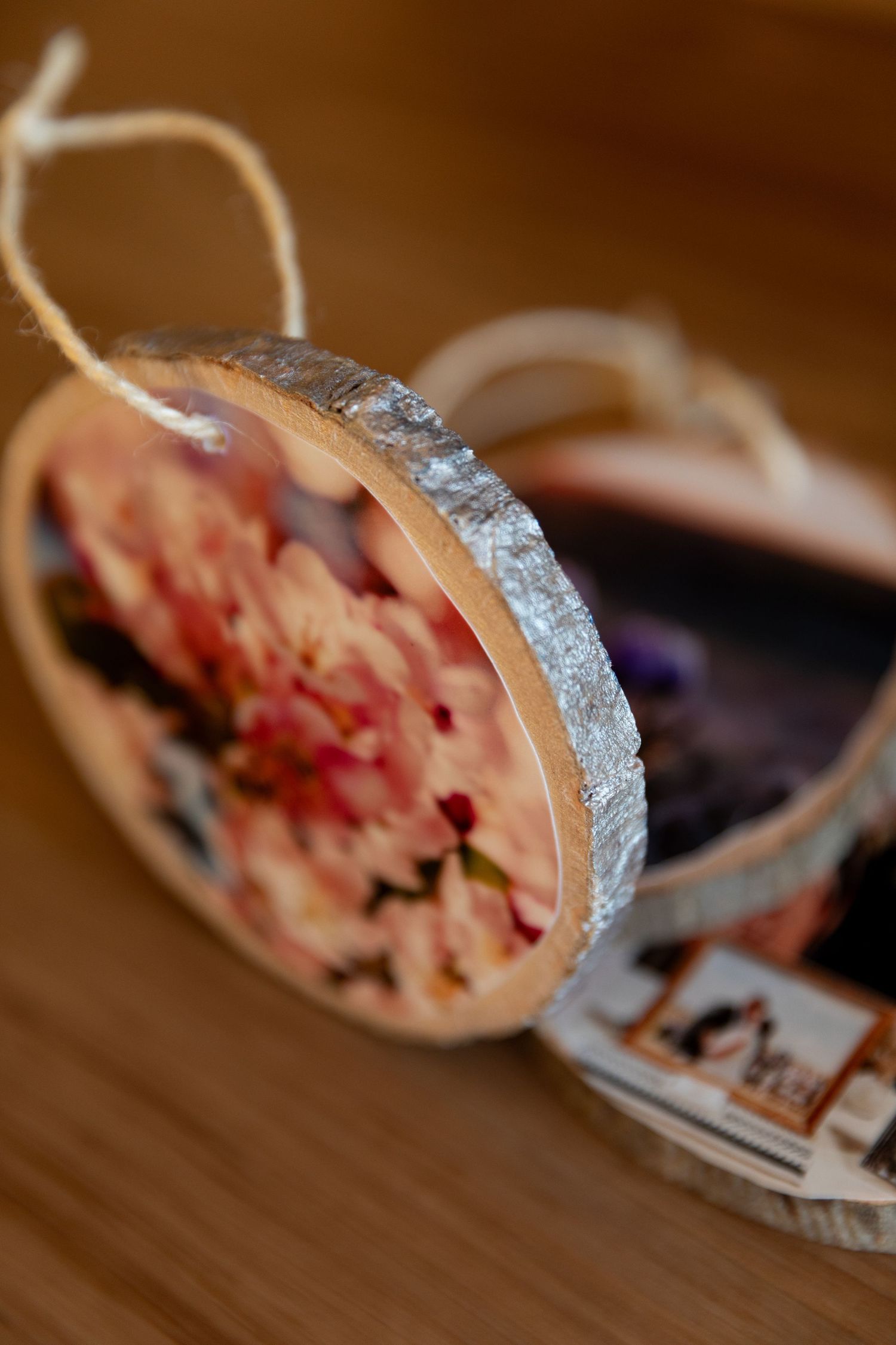 Close-up of a wooden slice ornament with silver-painted edges and dried flowers preserved inside.