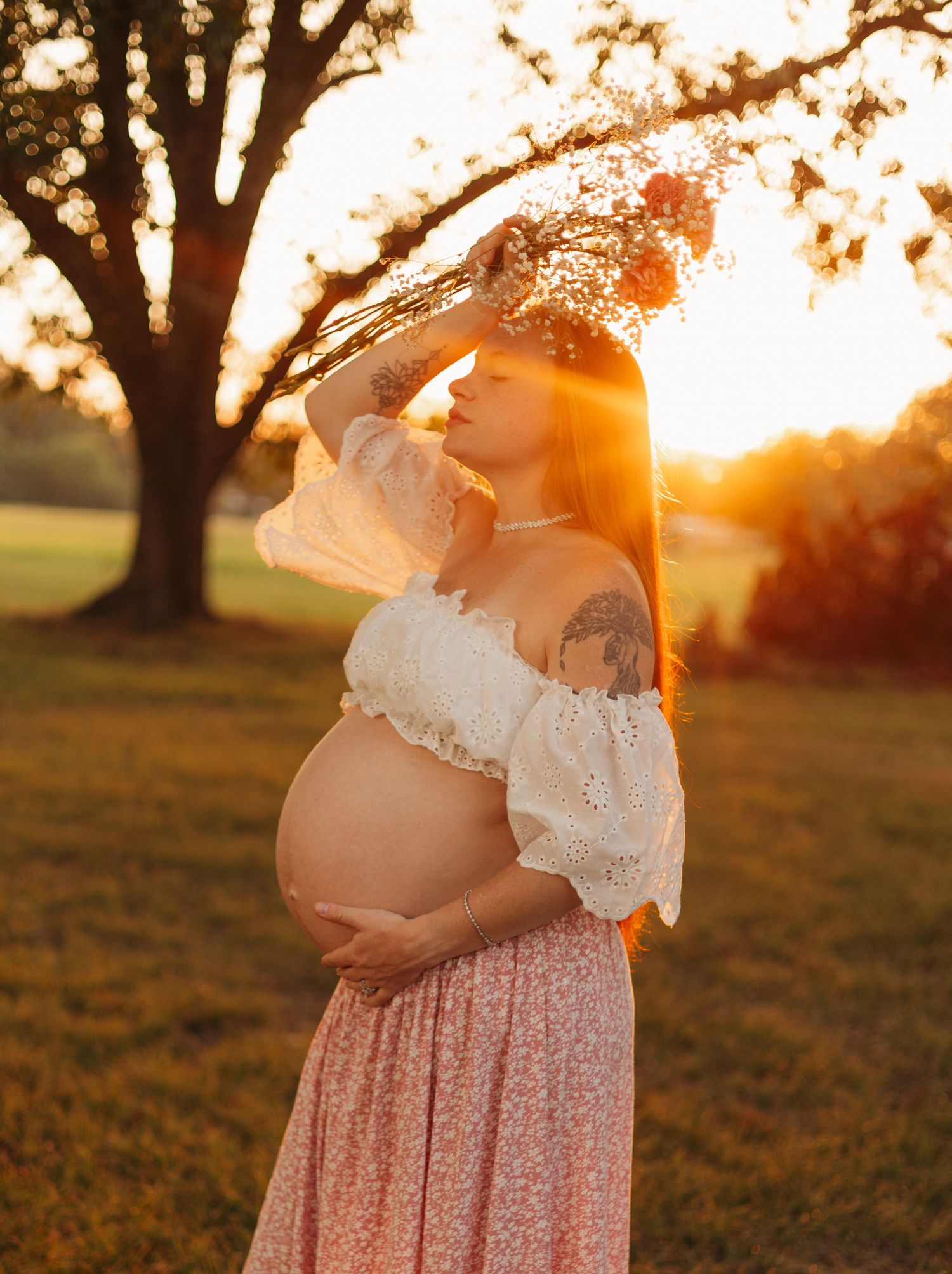 Pregnant mother posing outdoors at sunset with her hand on her baby bump during a golden-hour maternity photography session.